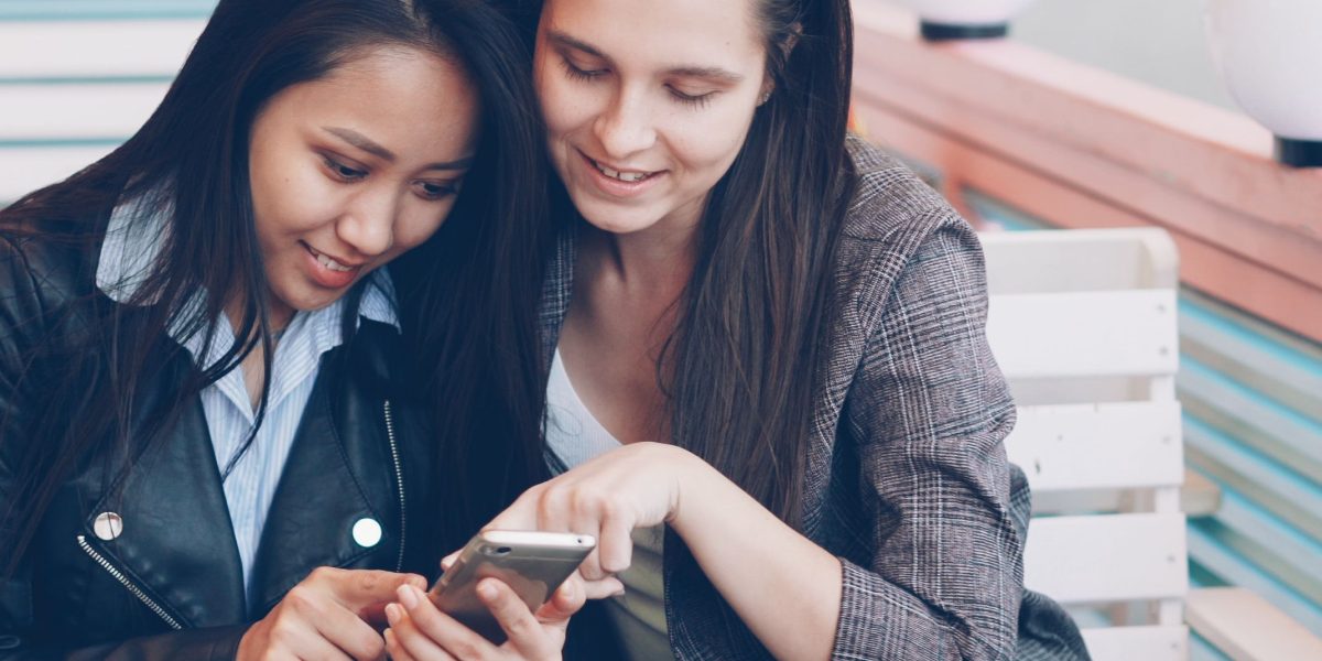 Friends share a moment of laughter while watching a humorous video on a phone.